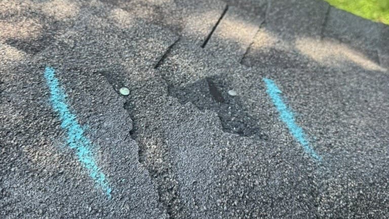 Real inspection photo of asphalt shingles with hail-impact mat exposure, full-depth fracture, and surrounding granule loss.